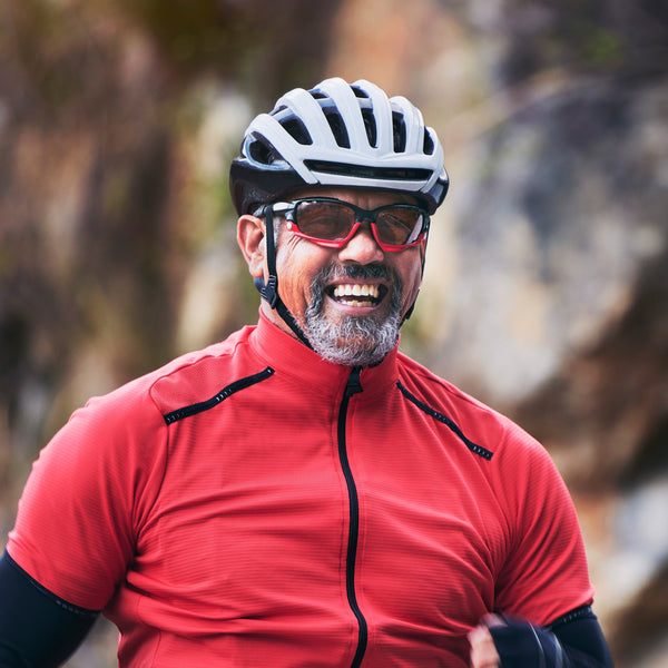 Smiling man in a red cycling jersey and helmet riding outdoors